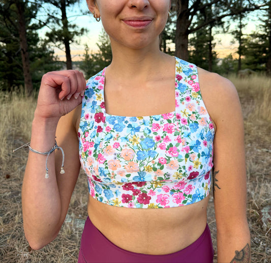 Woman wearing a floral sports bra and maroon leggings outdoors with trees in the background